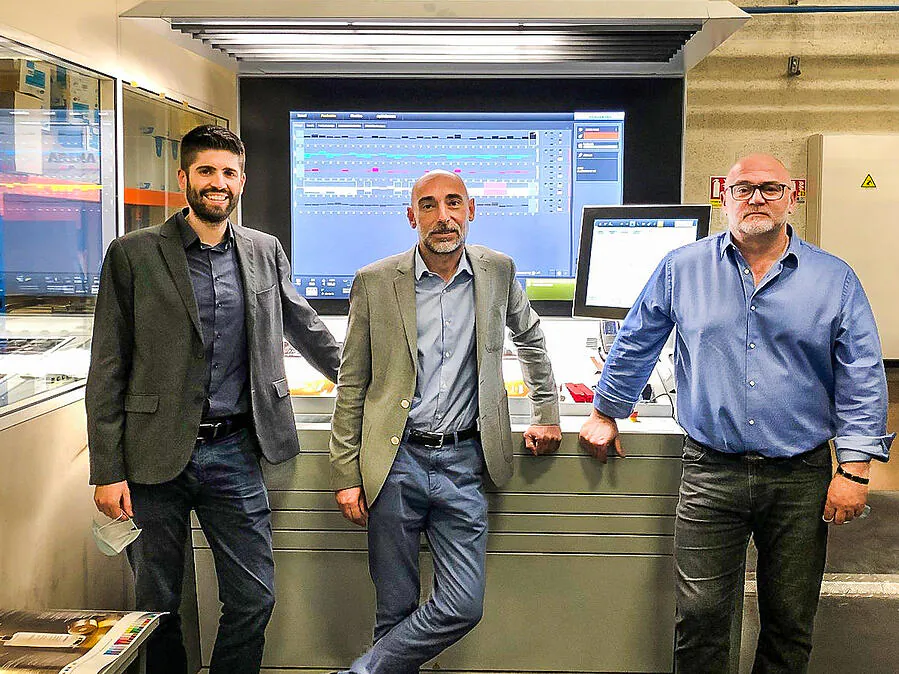 Three men standing at the control desk of a printing press